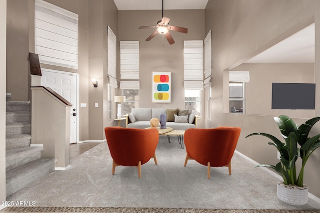 living room featuring a towering ceiling, light colored carpet, and ceiling fan