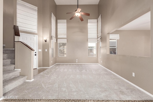 unfurnished living room featuring ceiling fan, carpet flooring, and a high ceiling