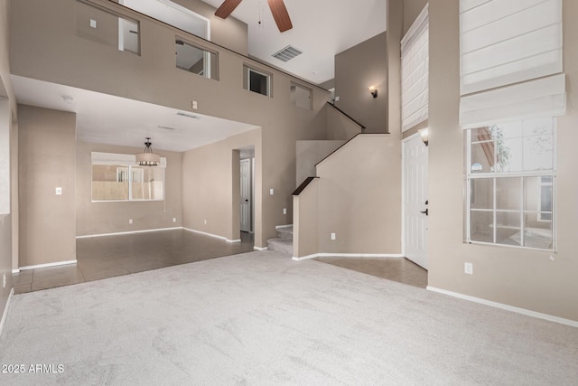 unfurnished living room featuring ceiling fan, a towering ceiling, and carpet flooring