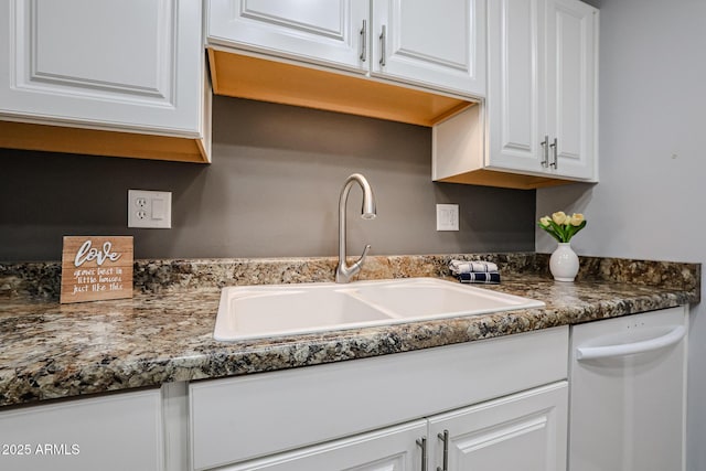kitchen with dark countertops, white dishwasher, a sink, and white cabinetry