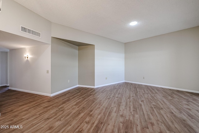 empty room with baseboards, wood finished floors, visible vents, and a textured ceiling