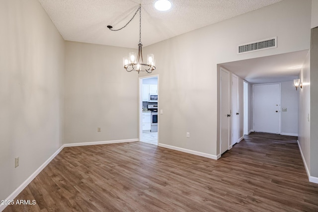 unfurnished dining area featuring wood finished floors, visible vents, baseboards, and a notable chandelier