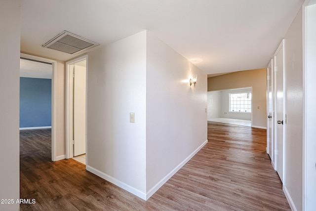 corridor with baseboards, wood finished floors, and visible vents