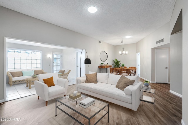 living room featuring a chandelier, wood finished floors, a textured ceiling, and visible vents