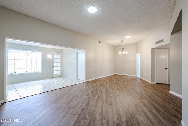interior space featuring wood finished floors, visible vents, a textured ceiling, and a notable chandelier