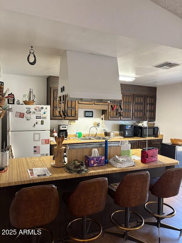 kitchen with wood-type flooring, white fridge, a breakfast bar, and sink