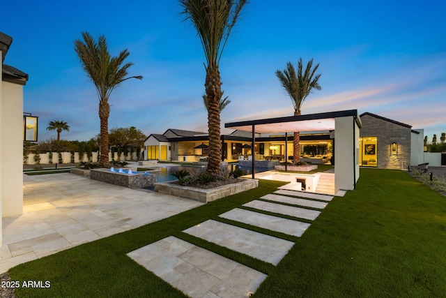 exterior space featuring exterior kitchen, a patio, stone siding, an infinity pool, and a lawn