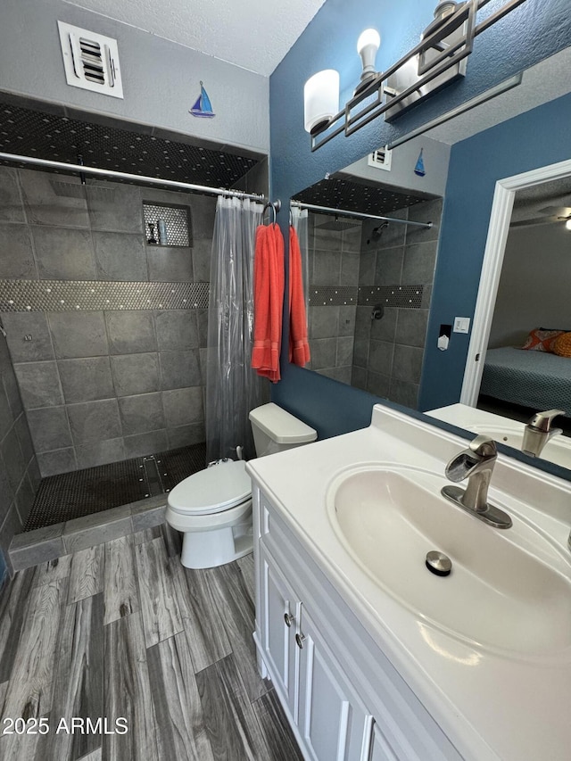 ensuite bathroom featuring a tile shower, toilet, visible vents, and wood finished floors