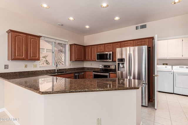 kitchen featuring light tile patterned flooring, kitchen peninsula, stainless steel appliances, separate washer and dryer, and dark stone counters