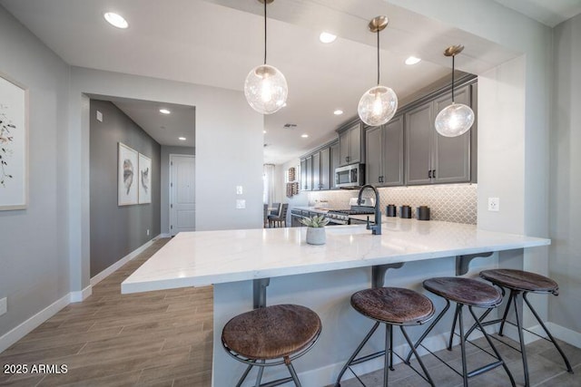 12239 W Caraveo Pl, Peoria, AZ 85383 - kitchen with appliances with stainless steel finishes, baseboards, a peninsula, gray cabinetry, and light wood finished floors