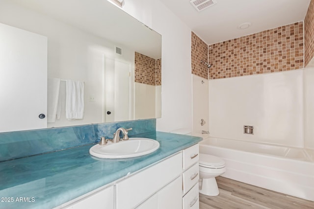 full bath featuring visible vents, toilet, wood finished floors, vanity, and washtub / shower combination