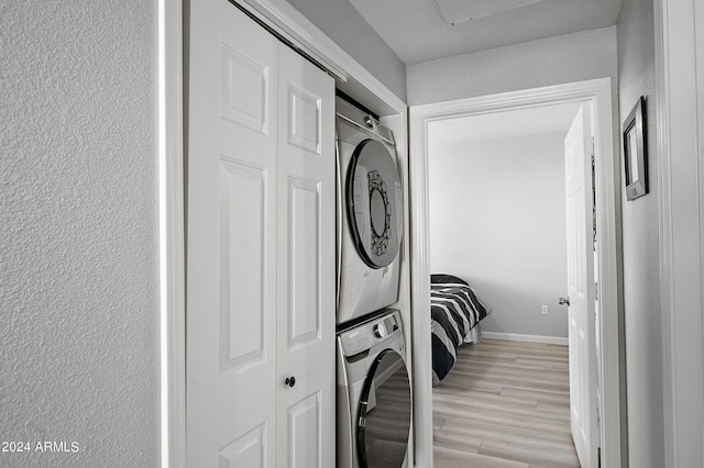 washroom with a textured wall, laundry area, baseboards, light wood-style floors, and stacked washer and clothes dryer