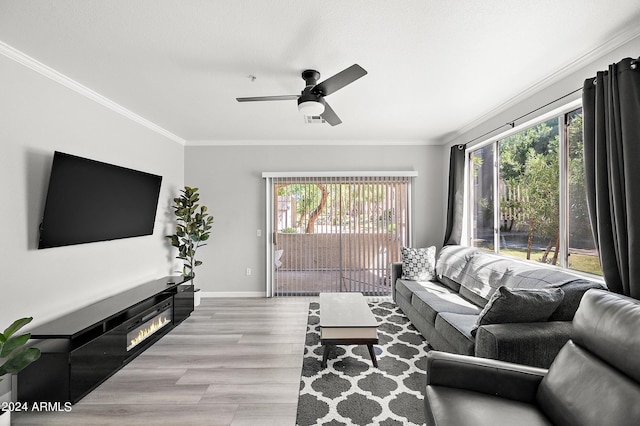 living area featuring baseboards, a glass covered fireplace, ceiling fan, wood finished floors, and crown molding