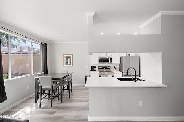 kitchen featuring a sink, white cabinetry, light wood-style floors, ornamental molding, and appliances with stainless steel finishes