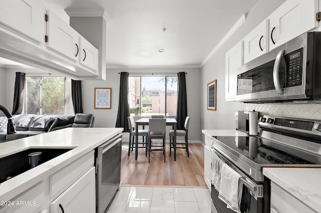 kitchen with baseboards, ornamental molding, stainless steel appliances, white cabinetry, and a sink