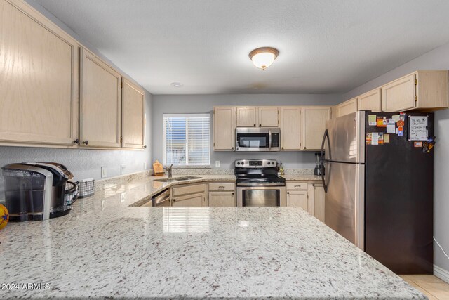 kitchen with kitchen peninsula, appliances with stainless steel finishes, light brown cabinets, and light stone counters