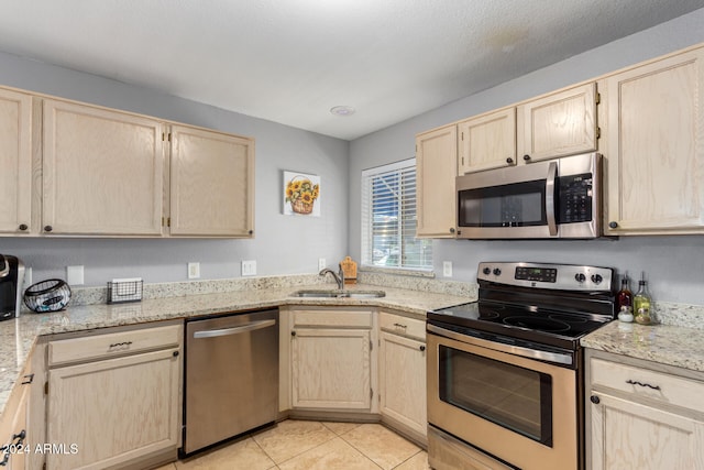 kitchen with light stone countertops, stainless steel appliances, sink, light brown cabinets, and light tile patterned floors