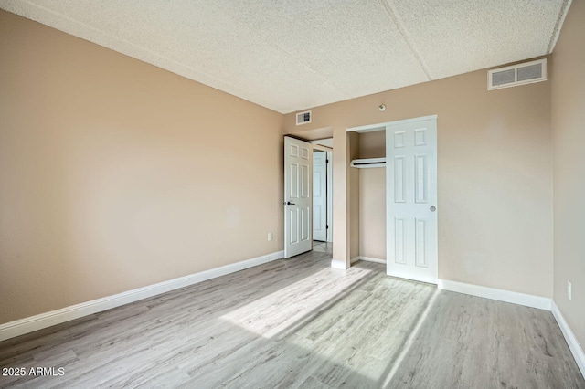 unfurnished bedroom with a textured ceiling, a closet, and light wood-type flooring