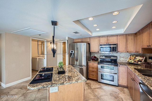 kitchen featuring stone counters, appliances with stainless steel finishes, washer and dryer, a center island, and a tray ceiling