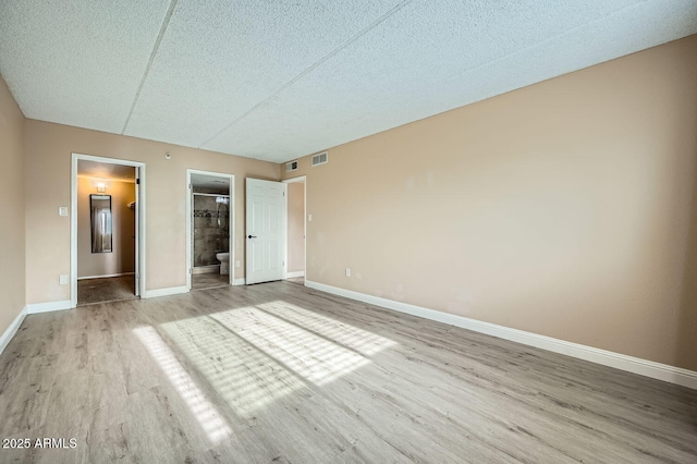 unfurnished bedroom with connected bathroom, a spacious closet, light hardwood / wood-style flooring, and a textured ceiling