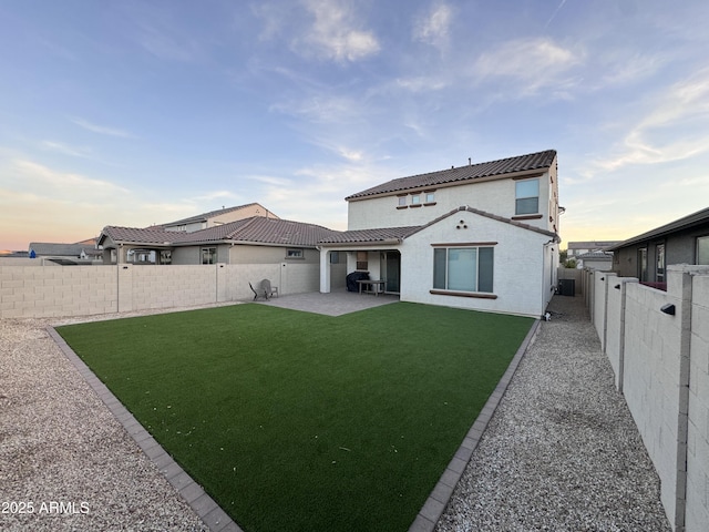 back house at dusk featuring a yard and a patio