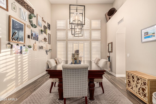 dining space featuring dark hardwood / wood-style floors, a towering ceiling, and an inviting chandelier