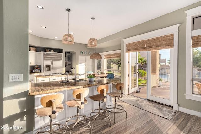 kitchen featuring built in fridge, pendant lighting, white cabinetry, dark stone counters, and sink