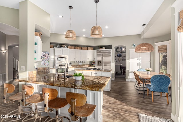 kitchen with white cabinets, pendant lighting, dark stone counters, and built in appliances