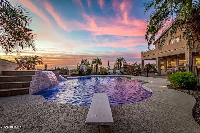 pool at dusk featuring a patio area, a diving board, and pool water feature