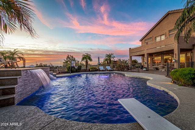 pool at dusk with a patio area, a diving board, and pool water feature