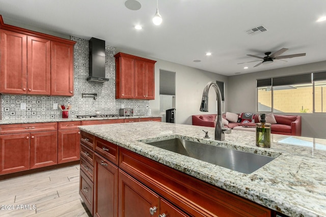 kitchen featuring sink, wall chimney exhaust hood, ceiling fan, light wood-type flooring, and light stone counters