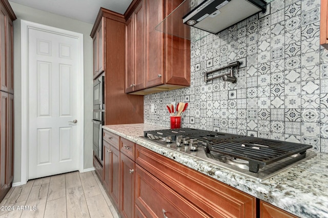 kitchen featuring light stone countertops, stainless steel appliances, ventilation hood, light hardwood / wood-style floors, and decorative backsplash