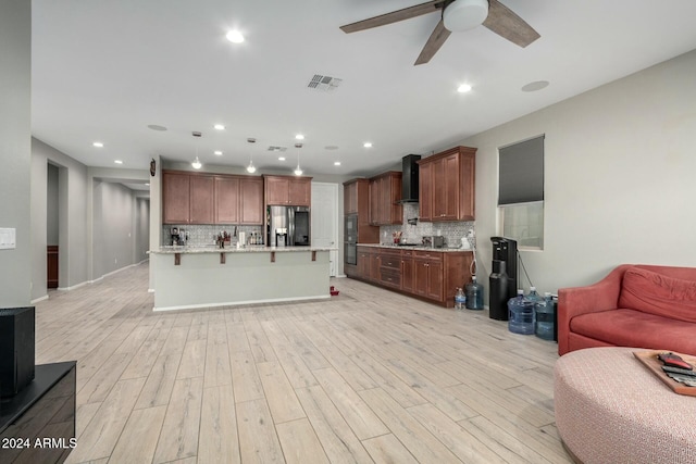 kitchen featuring stainless steel fridge, a center island with sink, light hardwood / wood-style floors, and wall chimney range hood