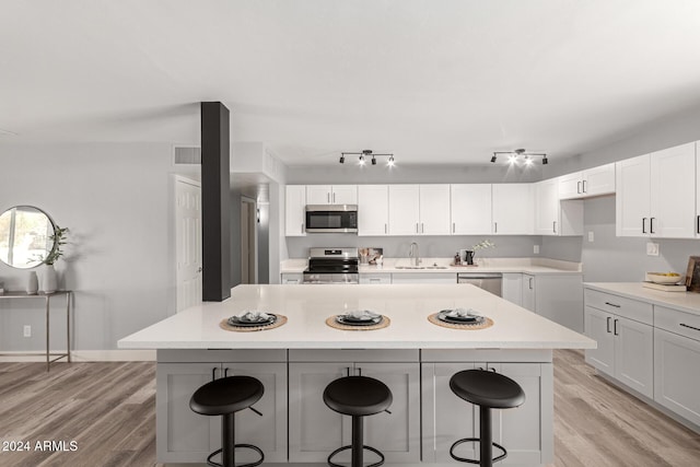 kitchen featuring appliances with stainless steel finishes, light wood-type flooring, white cabinetry, and a kitchen breakfast bar