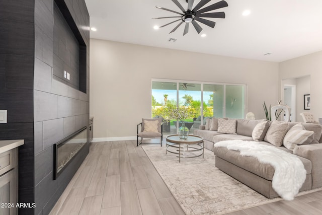 living room with ceiling fan, light hardwood / wood-style floors, and a tile fireplace