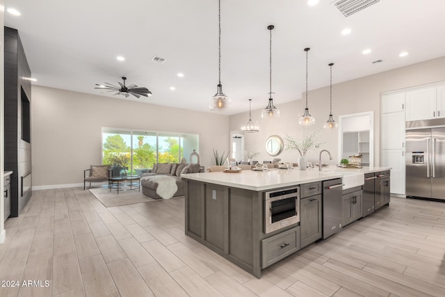 kitchen with light wood-type flooring, stainless steel appliances, ceiling fan, sink, and pendant lighting