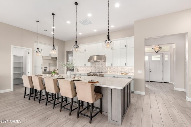 kitchen with a kitchen bar, stainless steel appliances, pendant lighting, a center island with sink, and white cabinets