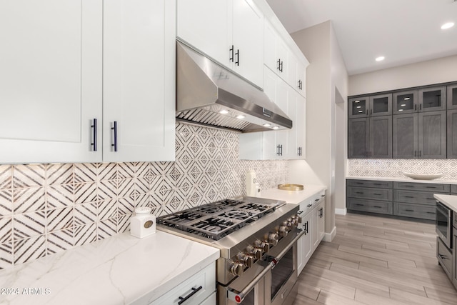 kitchen with light wood-type flooring, backsplash, light stone counters, range with two ovens, and white cabinets