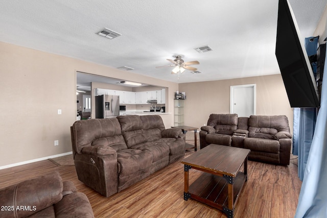 living room with a textured ceiling, light hardwood / wood-style flooring, and ceiling fan