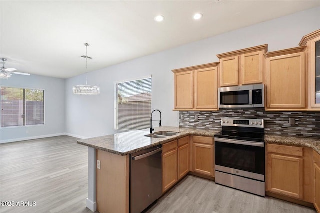 kitchen featuring kitchen peninsula, appliances with stainless steel finishes, tasteful backsplash, sink, and hanging light fixtures