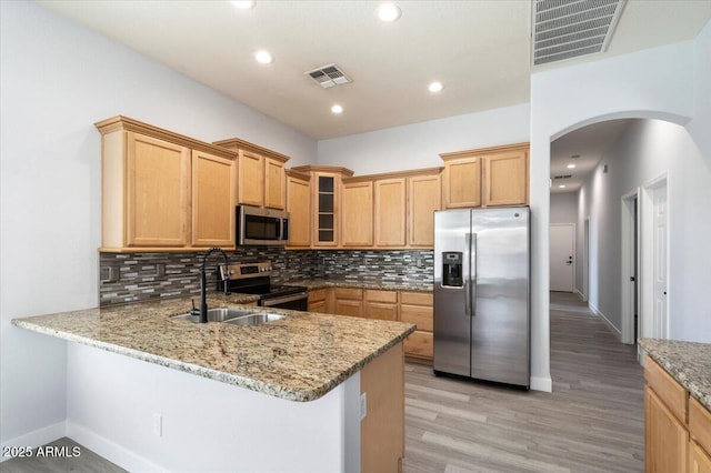 kitchen with kitchen peninsula, light stone counters, sink, and appliances with stainless steel finishes