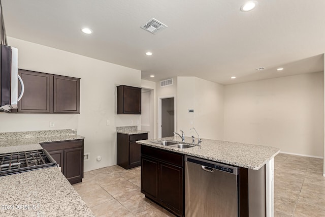 kitchen with dark brown cabinets, a center island with sink, appliances with stainless steel finishes, light stone countertops, and sink