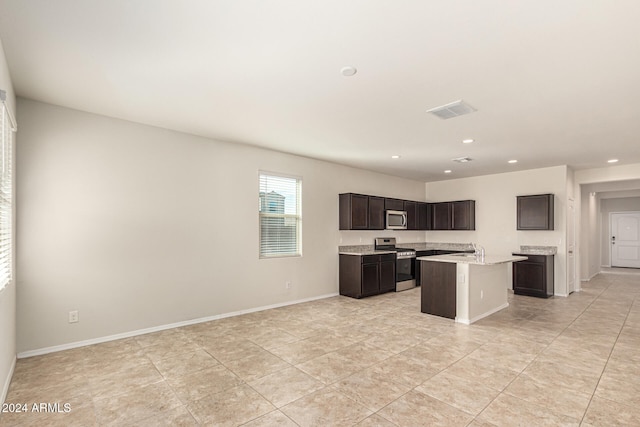 kitchen with dark brown cabinetry, stainless steel appliances, light tile patterned floors, and an island with sink