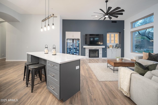 kitchen with gray cabinetry, hanging light fixtures, hardwood / wood-style flooring, a kitchen island, and beverage cooler