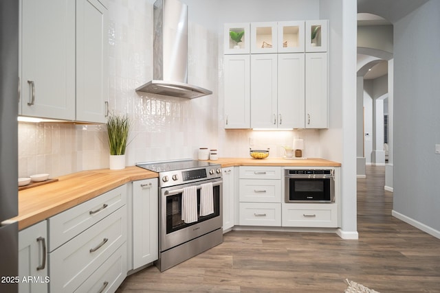 kitchen with butcher block counters, white cabinetry, wall chimney exhaust hood, stainless steel appliances, and dark hardwood / wood-style floors