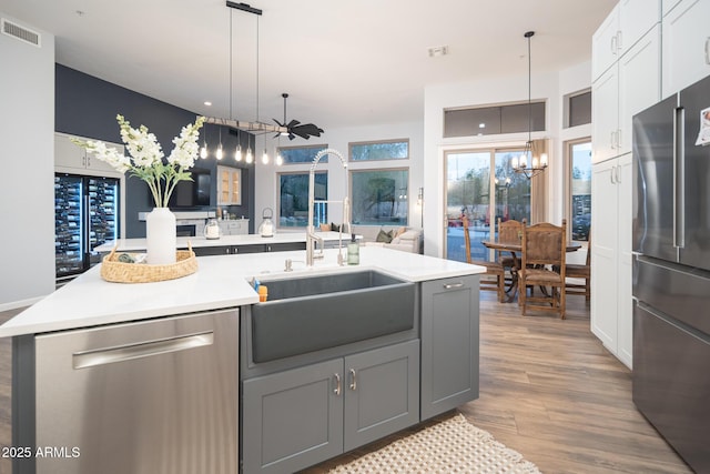 kitchen with sink, stainless steel appliances, gray cabinets, a kitchen island with sink, and ceiling fan with notable chandelier