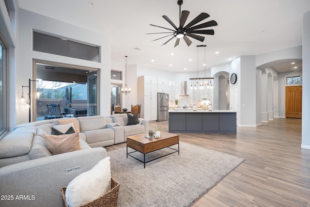 living room with ceiling fan with notable chandelier and light hardwood / wood-style floors