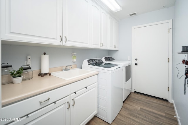 laundry area featuring hardwood / wood-style flooring, cabinets, sink, and washing machine and dryer