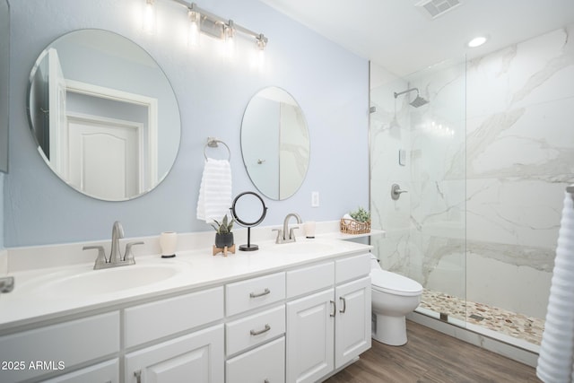 bathroom featuring toilet, vanity, wood-type flooring, and tiled shower