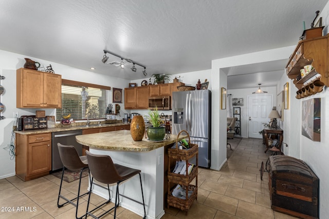 kitchen featuring a textured ceiling, a center island, a kitchen breakfast bar, stainless steel appliances, and light tile patterned floors